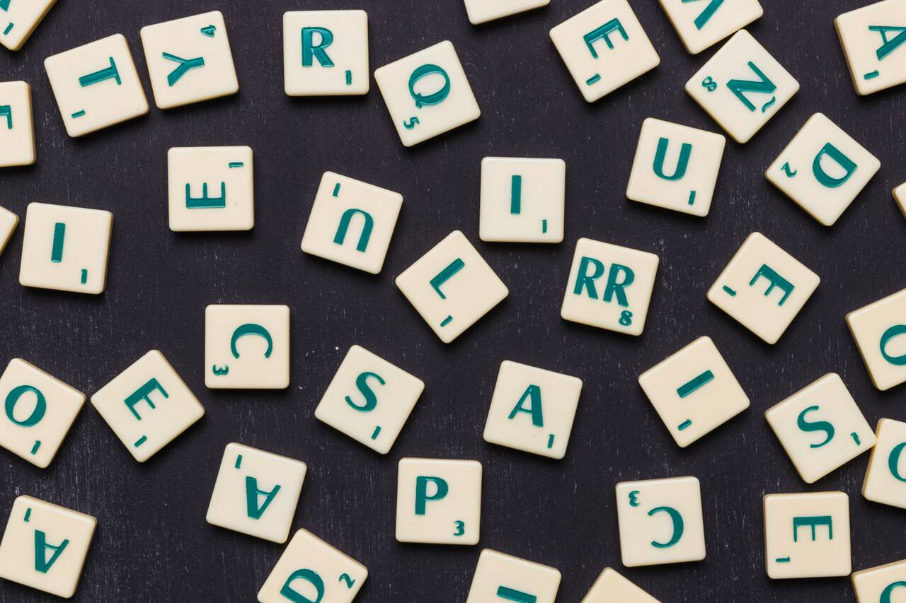 Scattered letter tiles on a dark surface, resembling a Scrabble game.