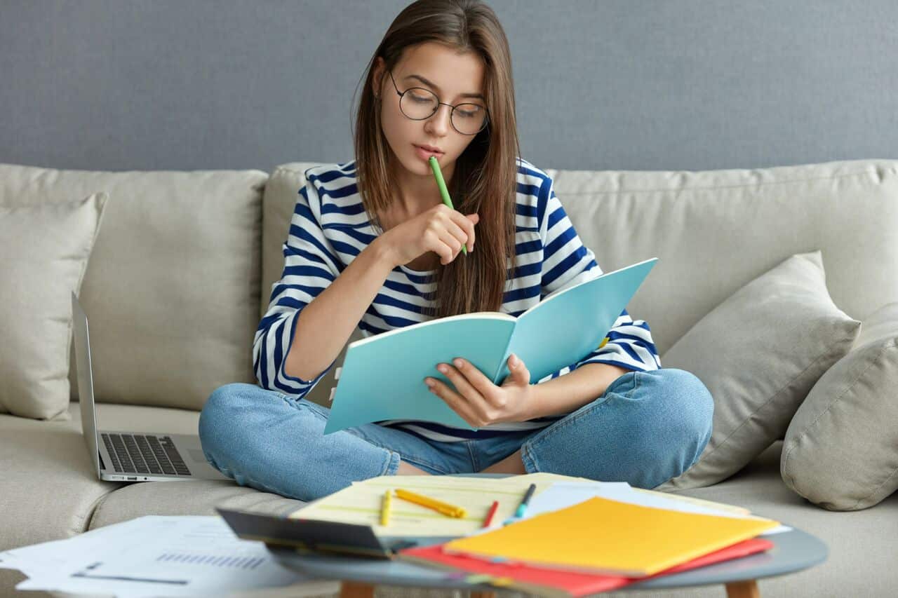 Woman studying on sofa while reading notebook