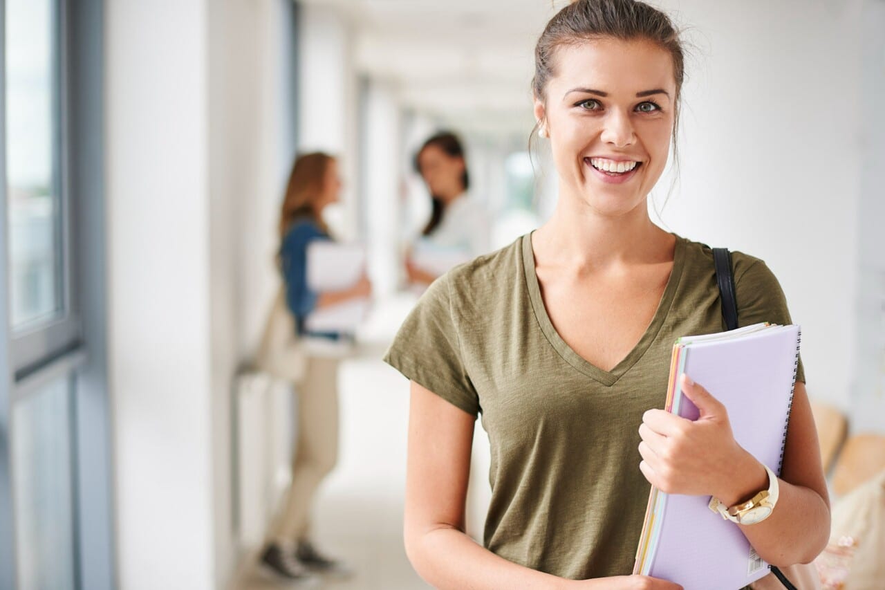 Smiling student holding notebooks in a hallway