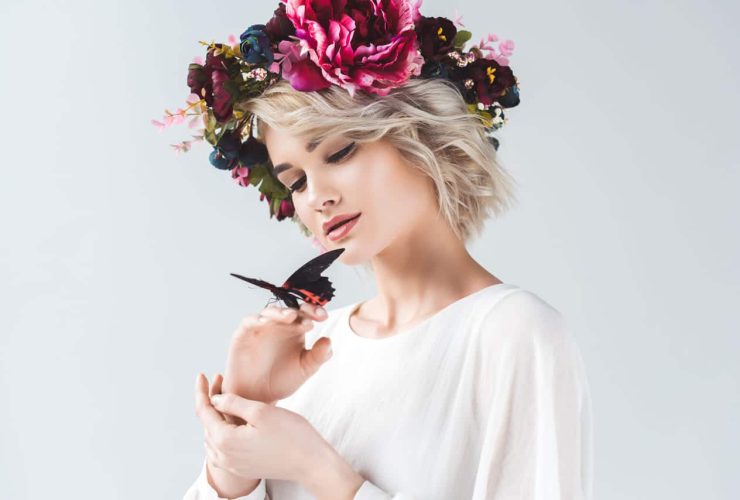 Woman with a floral crown holding a butterfly gently