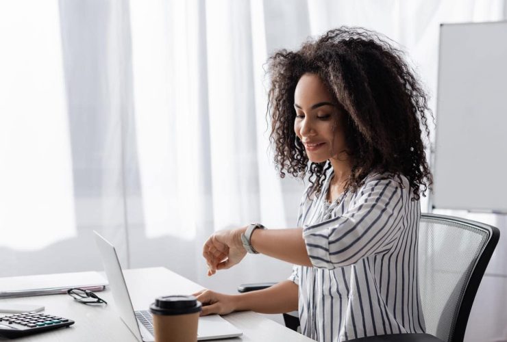 Woman checking her watch while working on a laptop