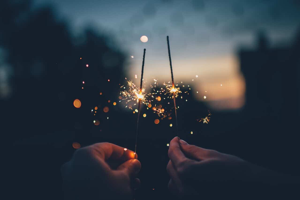 Two hands holding sparklers in the evening sky