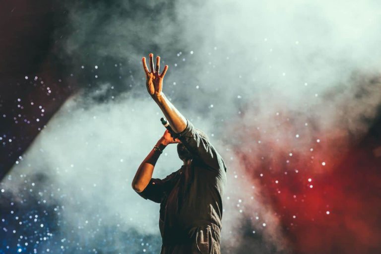 A performer on stage, holding a microphone and raising their hand toward the audience