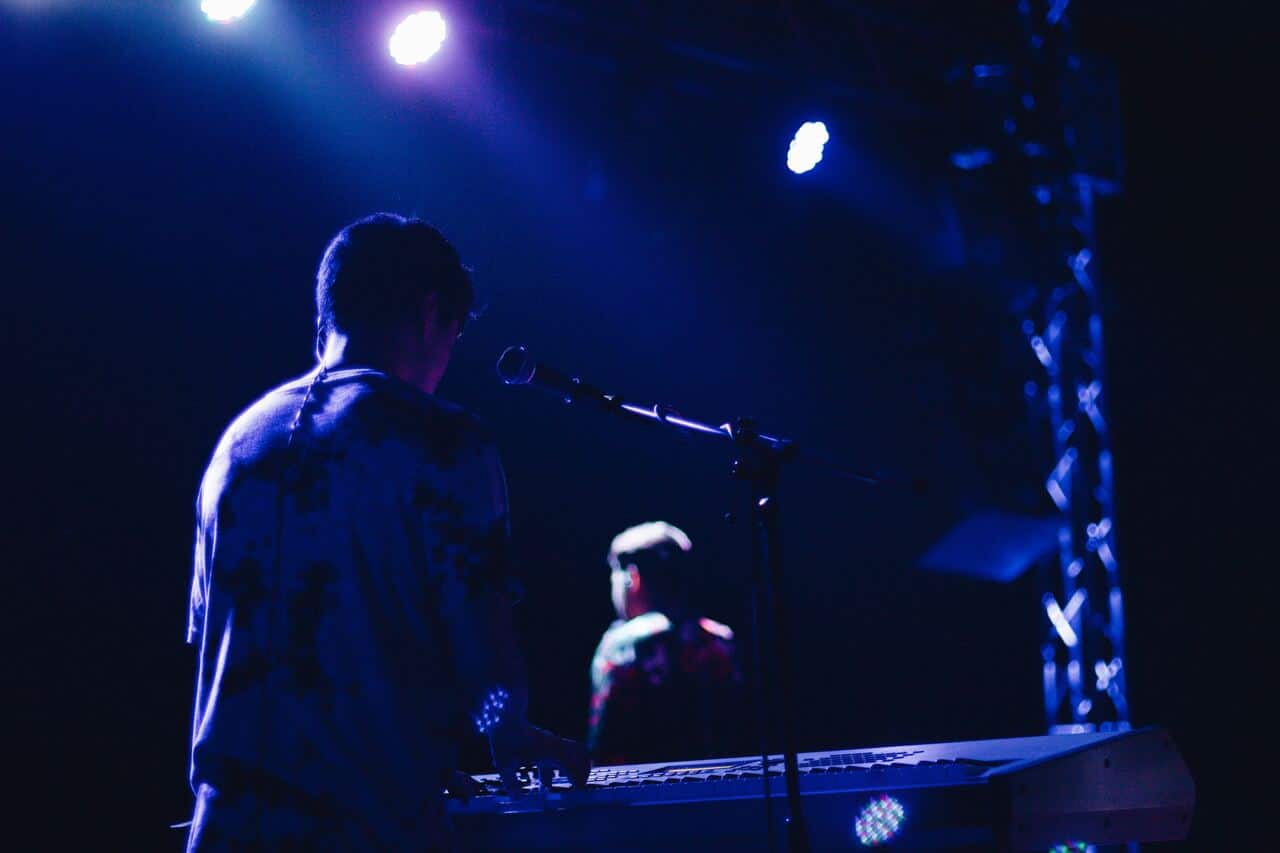 Performer playing keyboard on stage under blue lighting