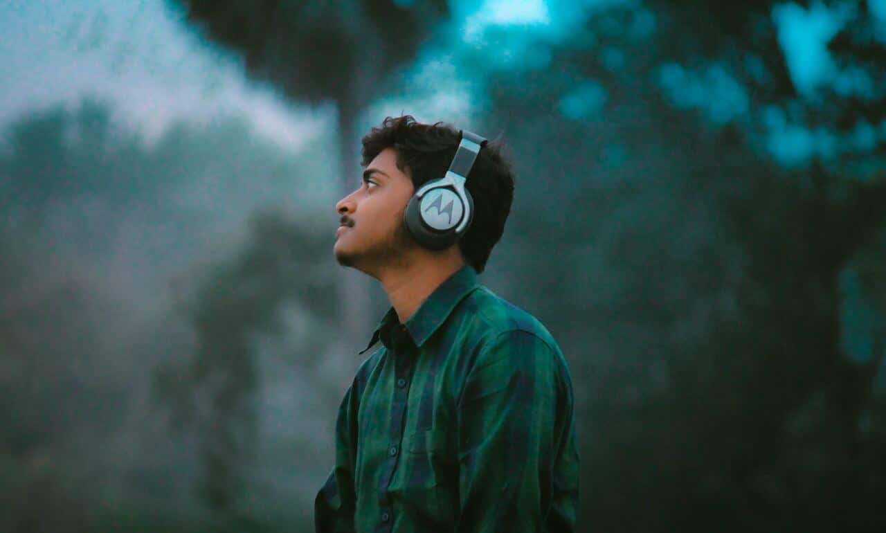 A man wearing headphones, gazing thoughtfully into the distance, against a misty, forested background.