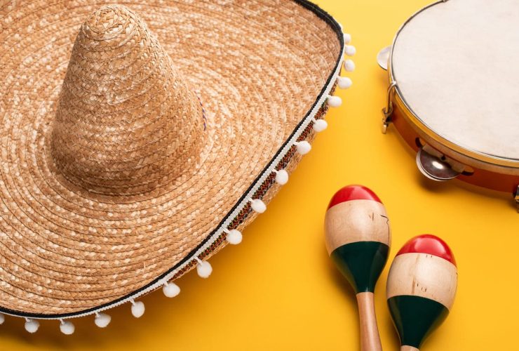 A straw sombrero, tambourine, and maracas on a yellow background.