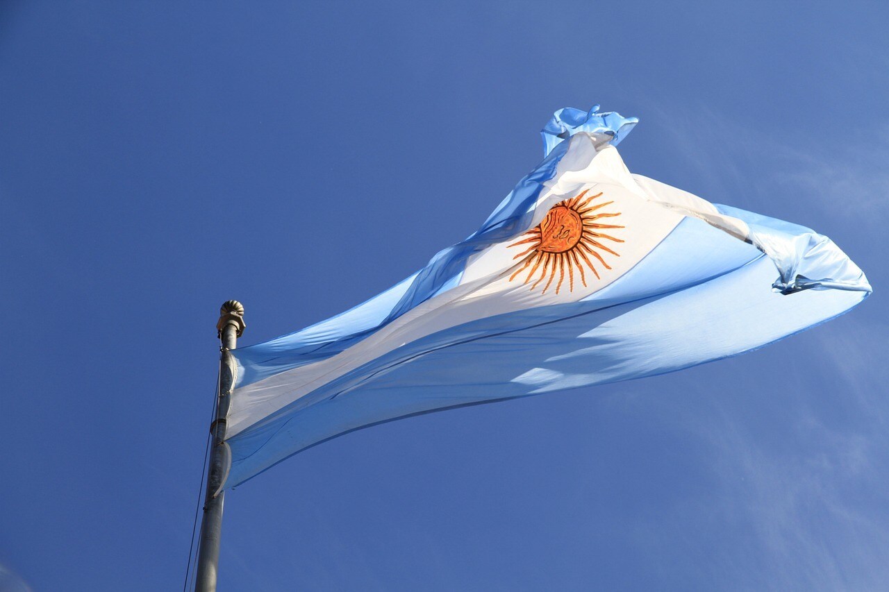 The flag of Argentina, featuring the Sun of May symbol against blue and white stripes, flying against a clear blue sky.