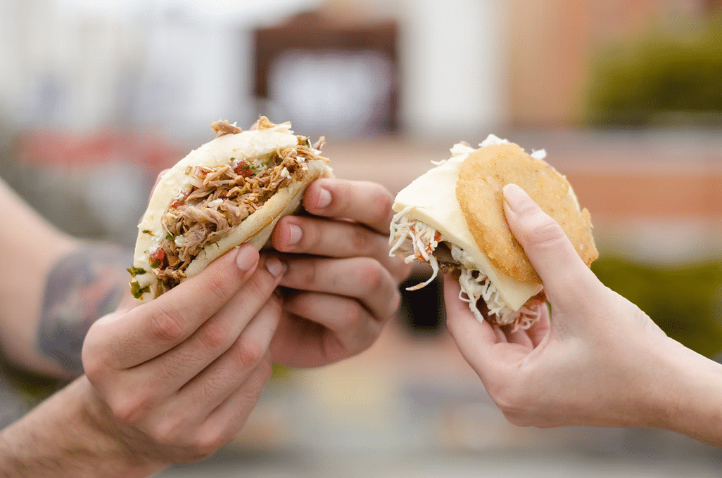 Two people holding Venezuelan arepas filled with different ingredients