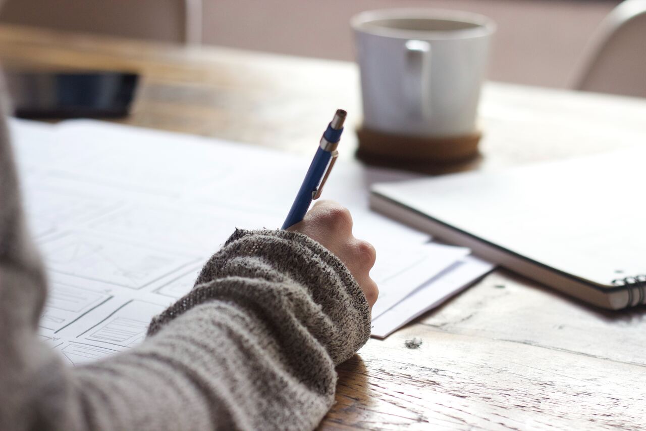 Person writing on paper with pen, coffee nearby