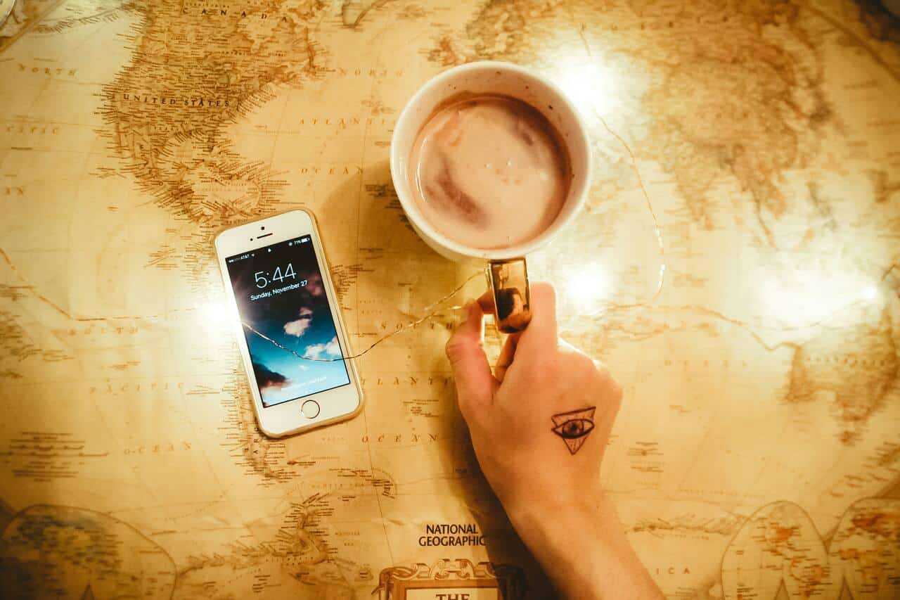 Hand holding coffee mug beside phone on world map