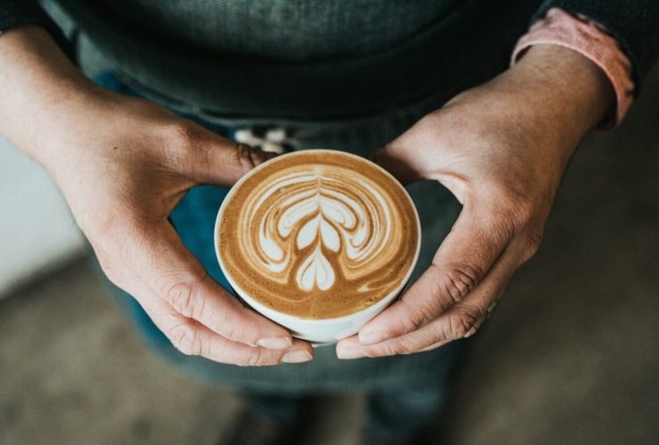 Hands holding a latte with intricate foam art