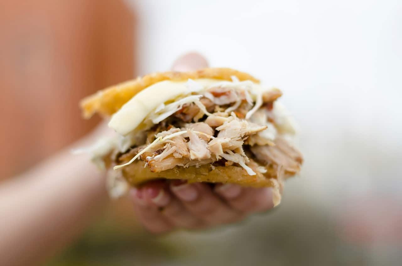 Close-up of a hand holding a pulled pork sandwich with cheese and shredded cabbage, ready to eat