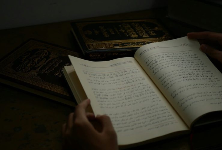 Person reading Arabic text from an open book.