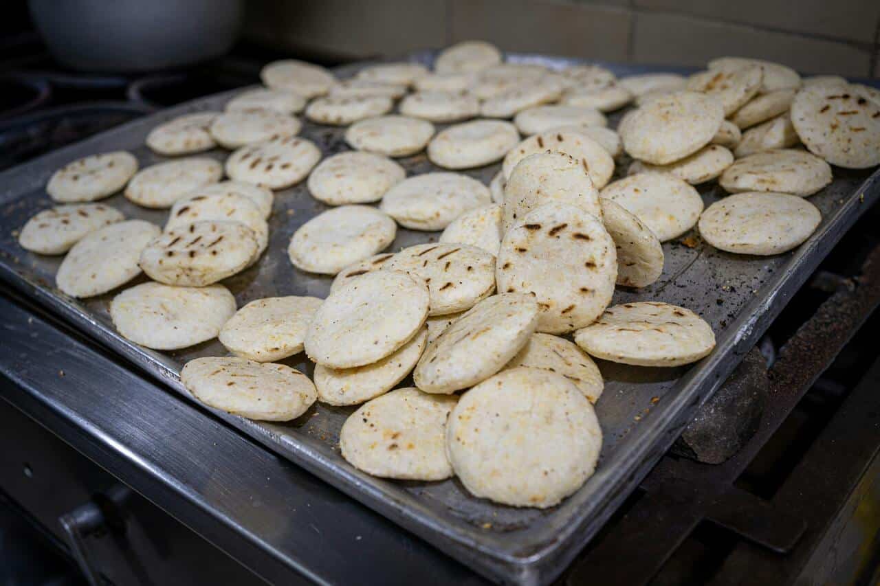 Dozens of small, grilled arepas on a metal tray, freshly cooked and ready to be served