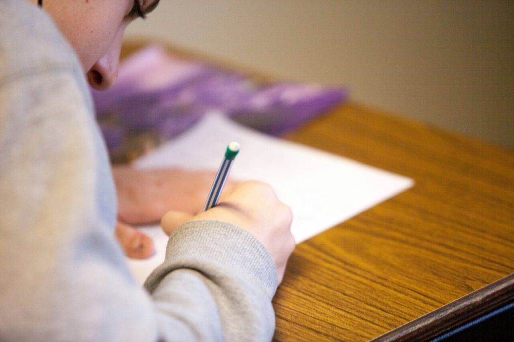 Student focusing on writing with a pencil on paper, sitting at a wooden desk during a study session.