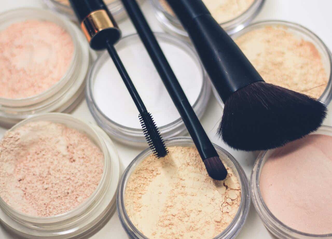 Assorted loose face powders in containers with makeup brushes and a mascara wand arranged on top