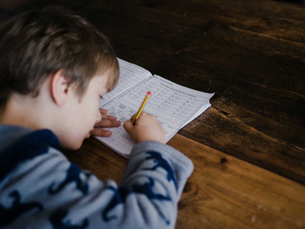 Child focused on completing a worksheet with a pencil, resting their head on the table while writing.