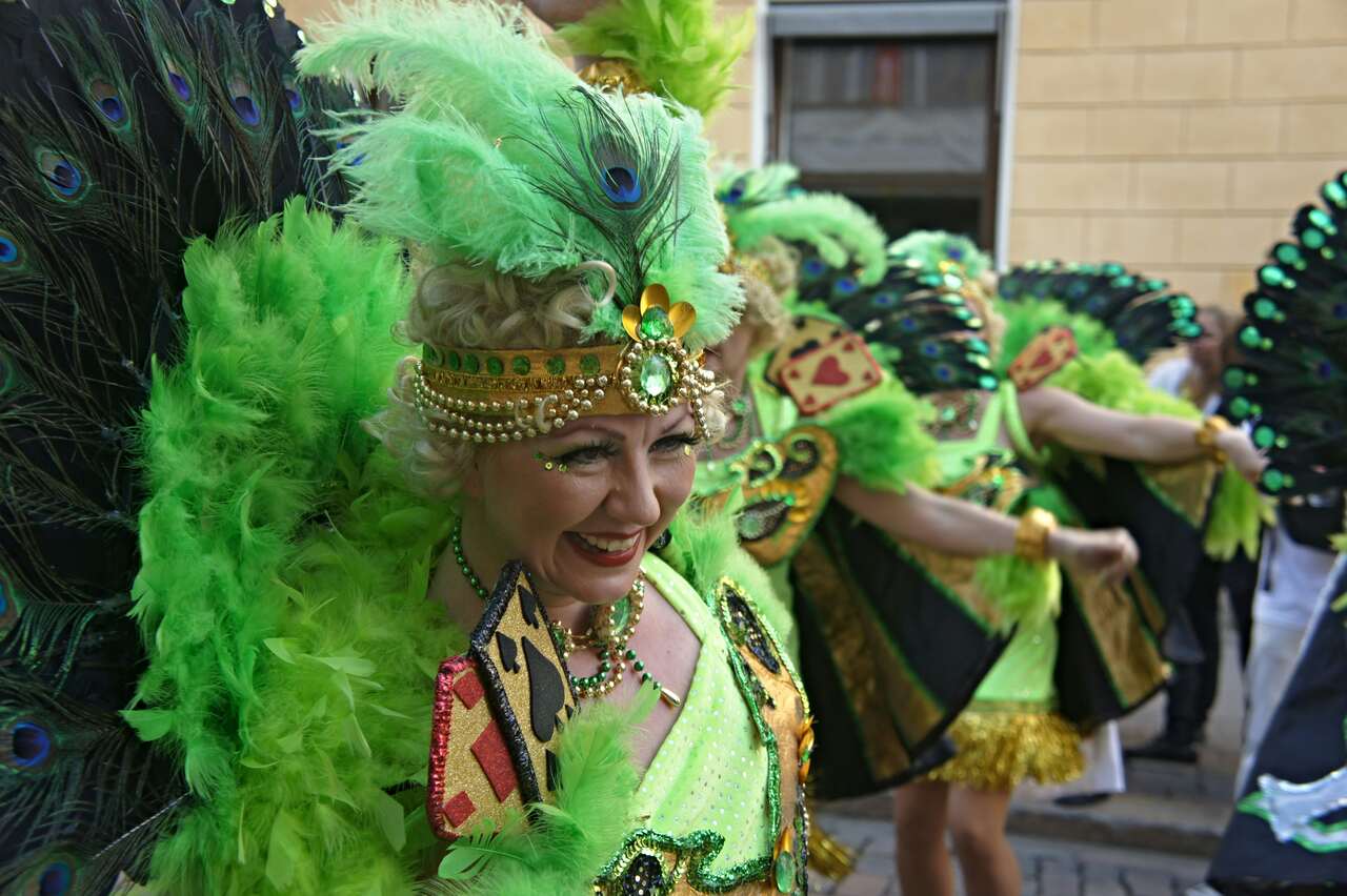 Women in vibrant green feathered costumes smiling during a festive parade with detailed peacock designs