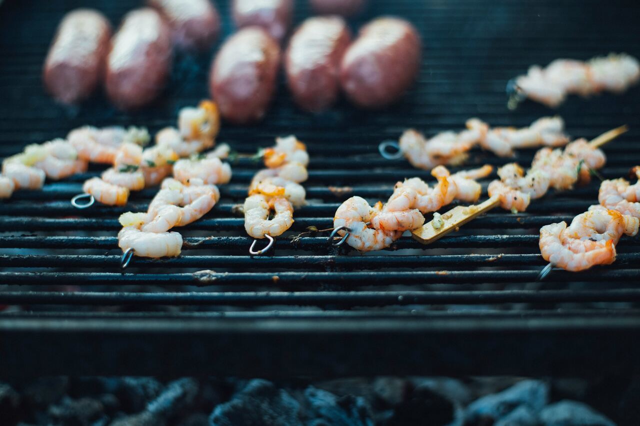 Shrimp skewers grilling on a barbecue, alongside sausages, over hot charcoal.