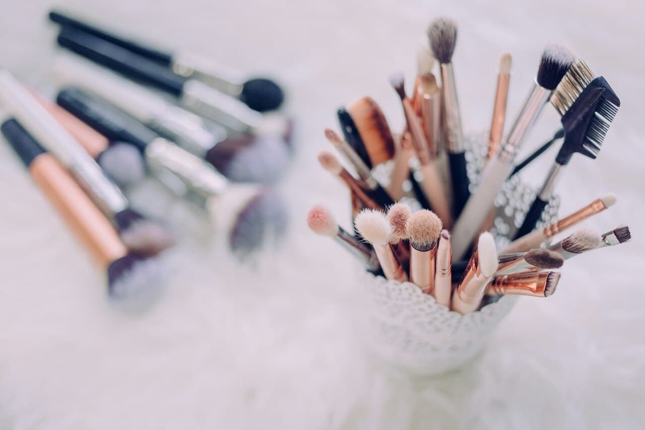 Various makeup brushes arranged in a decorative cup, with additional brushes scattered on a soft surface