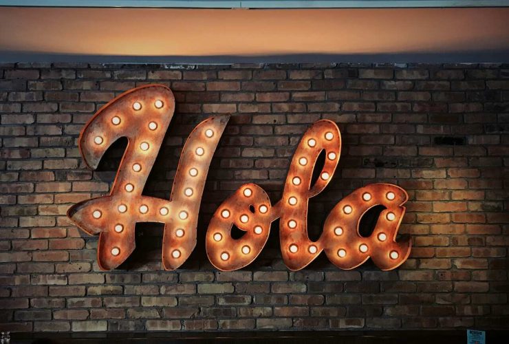 Illuminated ‘Hola’ sign with light bulbs mounted on a rustic brick wall in a cozy setting