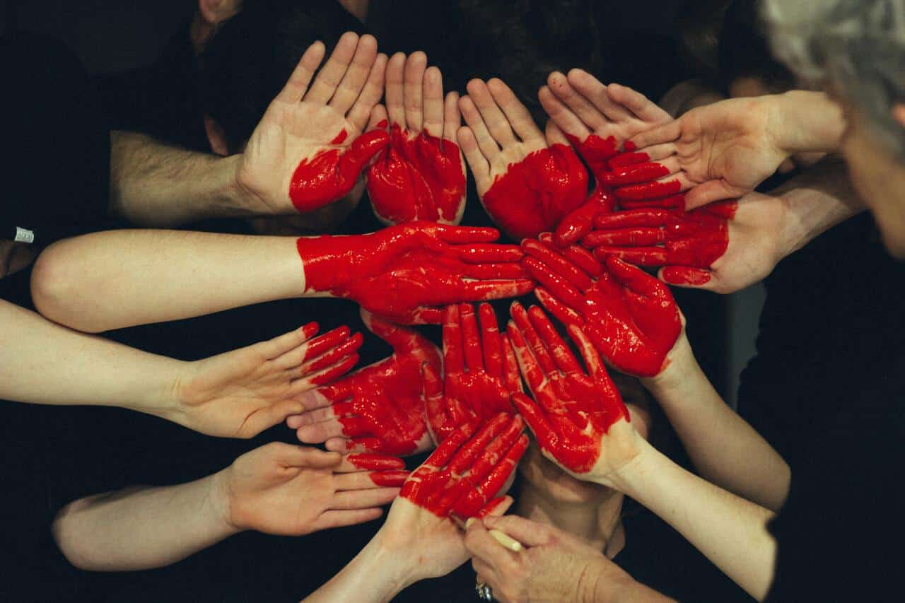 Group of hands painted with red, forming the shape of a heart, symbolizing unity and collaboration.